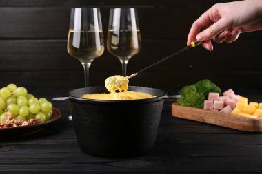 Siyah ahşap masada erimiş peynirle üzümü fondü kabına daldıran kadın, yakın plan.