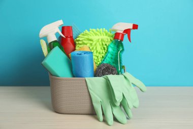 Tahta masadaki sepetteki farklı temizlik ürünleri açık mavi arka planda