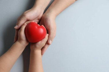 Anne ve çocuğunun elinde gri arka planda kırmızı dekoratif bir kalp var. Metin için boşluk