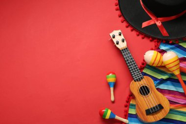 Meksika şapkası, marakas, gitar ve kırmızı arka planda renkli panço. Metin için boşluk