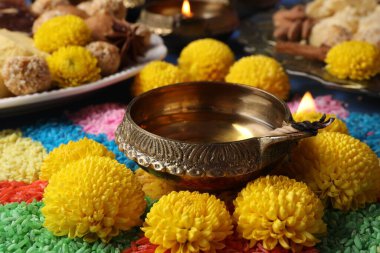 Diwali kutlaması. Diya lambası, renkli rangoli ve kasımpatı çiçekleri masada, yakın plan.
