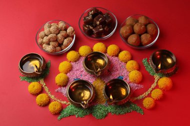 Mutlu bayramlar. Kırmızı masa üzerinde yeşil lambalar, rengarenk rangoliler, çiçekler ve lezzetli Hint tatlıları.