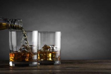 Gri arkaplana karşı tahta masada buzlu bardağa viski dökmek, yazı için yer açmak