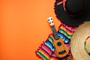 Meksika şapkası, gitar ve turuncu arka planda renkli panço, düz yatış. Metin için boşluk