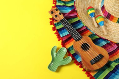 Üzerinde Meksika şapkası, ukulele ve marakas olan kompozisyon sarı masanın üstünde. Metin için boşluk