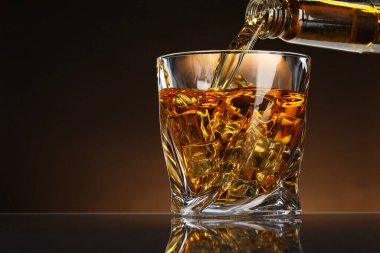 Viskiyi şişeden bardağa, masada buz küpleri ile kahverengi arka planda, mesaj için boşluk doldurmak