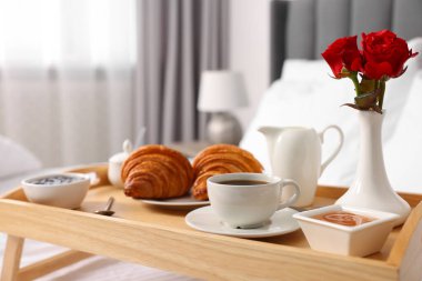 Yatakta servis edilen lezzetli kahvaltı. Taze kruvasanlar, kahve, reçel ve bal, ahşap tepside, yakın plan.