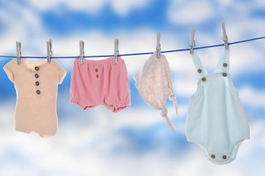 Different baby clothes drying on washing line against sky