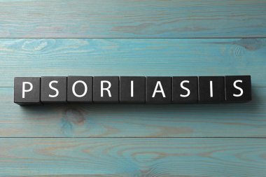 Kelime sedef hastalığı, mavi ışıklı ahşap masa üzerinde harflerle siyah küplerden yapılmıştır.