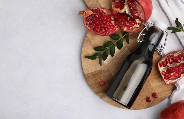 Tasty pomegranate sauce in bottle, branches and fruits on light table, flat lay. Space for text