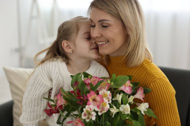 Küçük kız, annesini öpüyor ve tebrik ediyor evde bir buket alstromerya çiçeğiyle. Anneler Günün kutlu olsun.