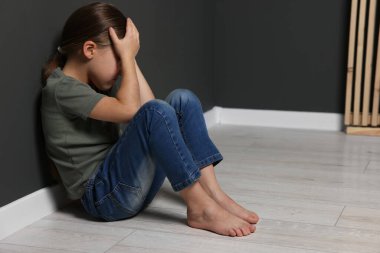 Çocuk istismarı. Üzgün kız gri duvarın yanında oturuyor, mesaj için yer var.