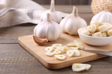 Aromatic cut garlic, cloves and bulbs on wooden table, closeup clipart