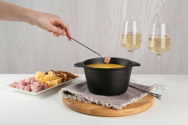 Beyaz masada erimiş peynirle fondü kabına jambon daldırmak.