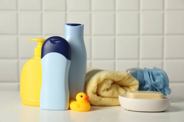 Bebek kozmetik ürünleri, banyo ördeği, sünger ve havlu beyaz masada fayanslı duvara karşı. Metin için boşluk