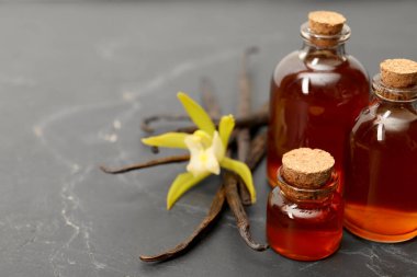 Aromatik vanilya özü, kapsüller ve çiçekler siyah masada, yakın plan. Metin için boşluk