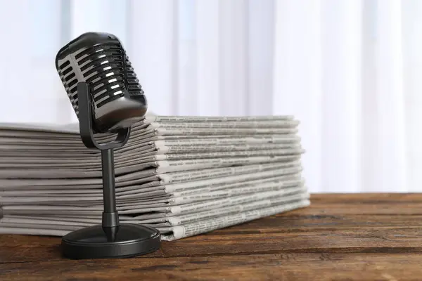 Newspapers and vintage microphone on wooden table. Journalist\'s work
