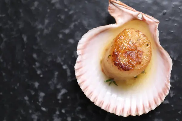 Delicious fried scallop in shell on black table, top view. Space for text