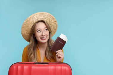 Pasaportu, bileti ve bavulu açık mavi arka planda olan mutlu genç kadın, mesaj için yer var.