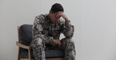 Stresli ordu subayı beyaz arka planda koltukta oturuyor.