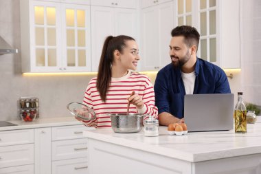 Mutfakta yemek yaparken dizüstü bilgisayar kullanan mutlu çift.