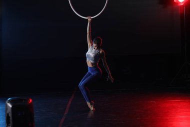 Genç bir kadın içerideki hava halkalarında akrobatik hareketler sergiliyor.