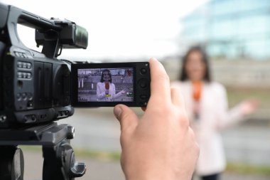 Şehir caddesinde çalışan genç erkek gazeteci ve video operatörü, kamera ekranına odaklanın