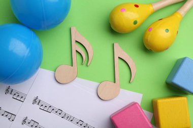 Bebek şarkıları yapmak için aletler. Düz kompozisyon, ahşap notalar ve yeşil arka planda marakas.