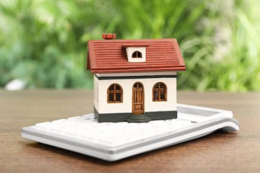 İpotek konsepti. Ev modeli ve hesap makinesi ahşap masa üzerinde bulanık yeşil arka plan, yakın plan