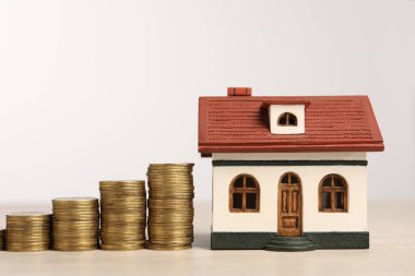 İpotek konsepti. Beyaz arka plana karşı ahşap masa üzerinde ev modeli ve madeni para yığınları