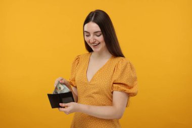 Mutlu kadın, turuncu arka planda cüzdanına para koyuyor.