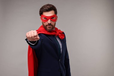 Kırmızı süper kahraman pelerini ve bej arka planda maske takan kendine güvenen bir iş adamı.