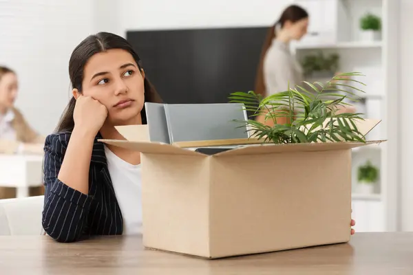Unemployment problem. Woman with box of personal belongings at table in office