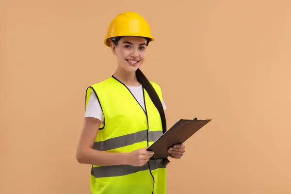 Engineer in hard hat holding clipboard on beige background