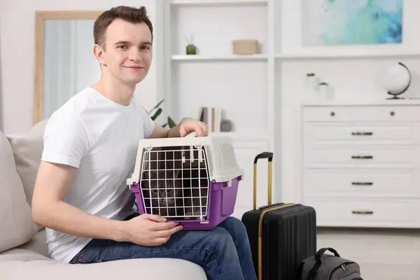 Travel with pet. Man holding carrier with cute cat on sofa at home, space for text