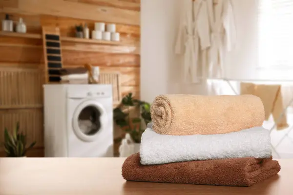Clean towels on wooden table in laundry room, space for text
