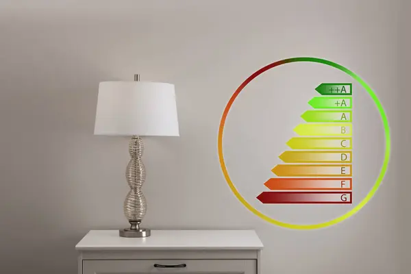 Energy efficiency rating label and lamp on bedside table near grey wall indoors