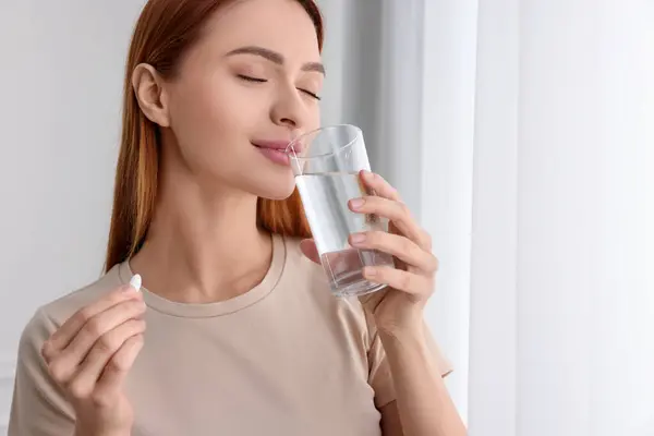 Beautiful young woman with vitamin pill and glass of water