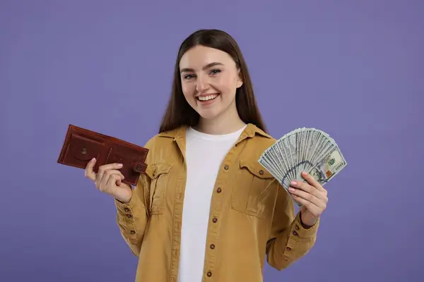 Happy woman with wallet and dollar banknotes on purple background