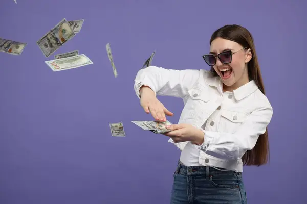 Happy woman throwing money on purple background