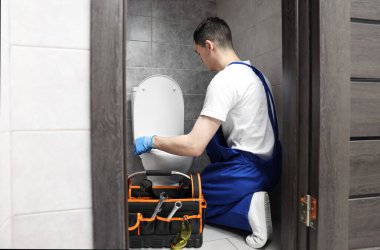 Su dolabında klozet tamir ederken koruyucu eldiven giyen genç bir tesisatçı.