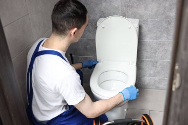 Su dolabında klozet tamir ederken koruyucu eldiven giyen genç bir tesisatçı.