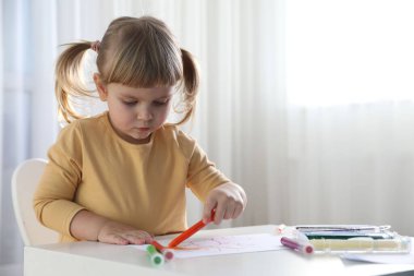 Beyaz masa içinde keçeli kalemle çizen şirin küçük kız. Çocuk sanatı