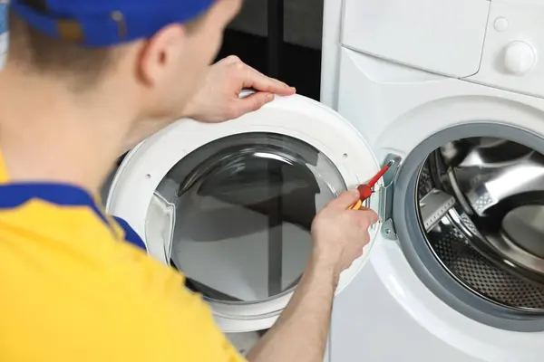 Plumber repairing washing machine with screwdriver indoors, closeup