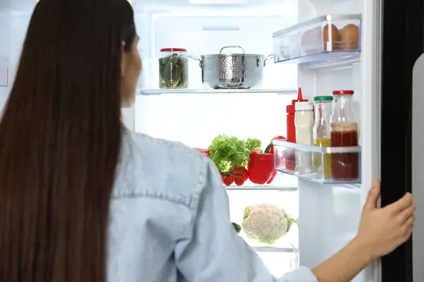 Young woman near modern refrigerator, selective focus