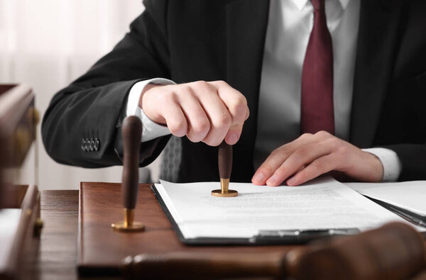 Notary stamping document at wooden table in office, closeup