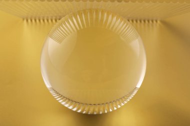 Sarı arka planda şeffaf cam top, yakın plan.