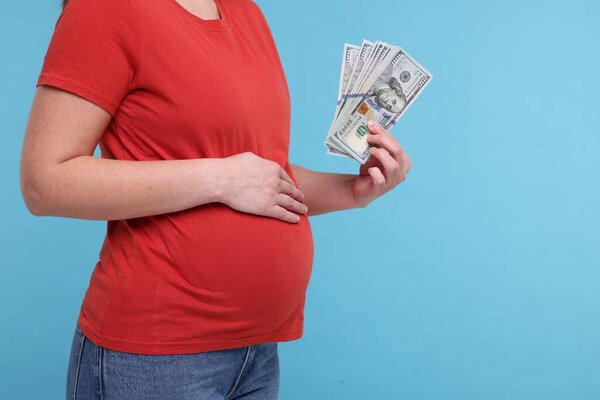 Surrogate mother. Pregnant woman with dollar banknotes on light blue background, closeup. Space for text