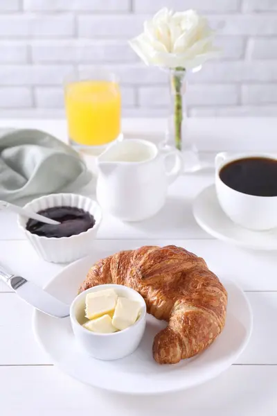 Fresh croissant, butter, jam and coffee on white wooden table. Tasty breakfast