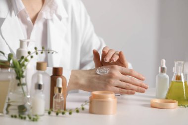 Dermatolog, beyaz masada el kremi sürüyor, yakın plan. Kozmetik ürünü test ediliyor